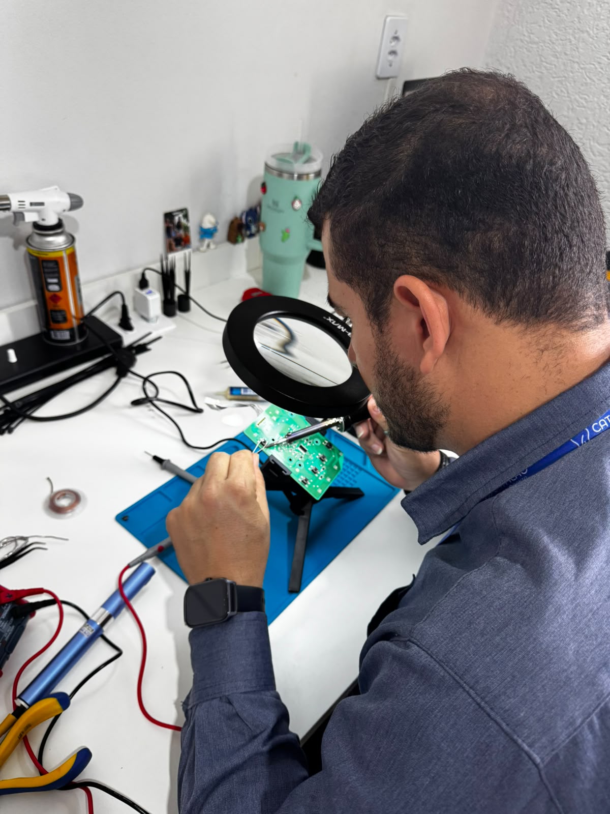 Trabalho com placa eletrônica, lupa e ferramentas de bancada.
